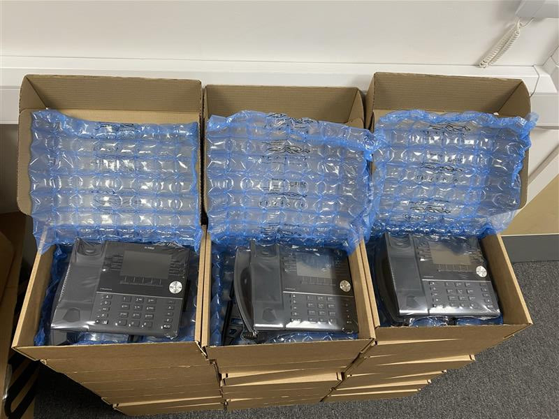 Stack of cardboard boxes with bubble wrap padding, containing refurbished Mitel IP Phones.